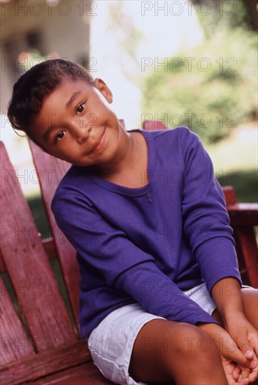 Cute young girl sitting outdoors on chair in summer. Photo : Rob Lewine