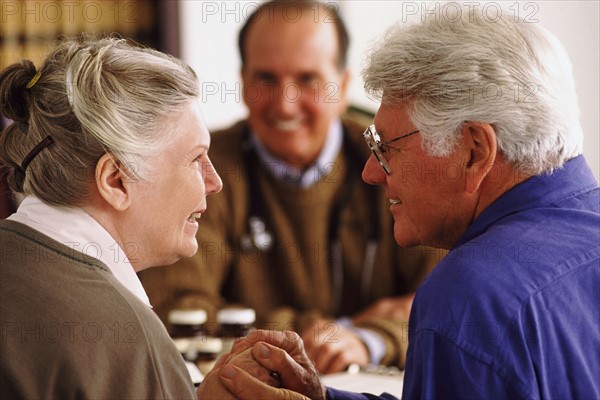 Senior couple sitting at desk across from doctor. Photo : Rob Lewine