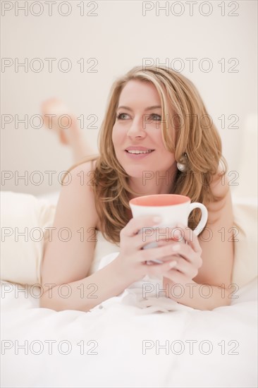 Woman lying down with a cup of coffee. Photo : Dan Bannister