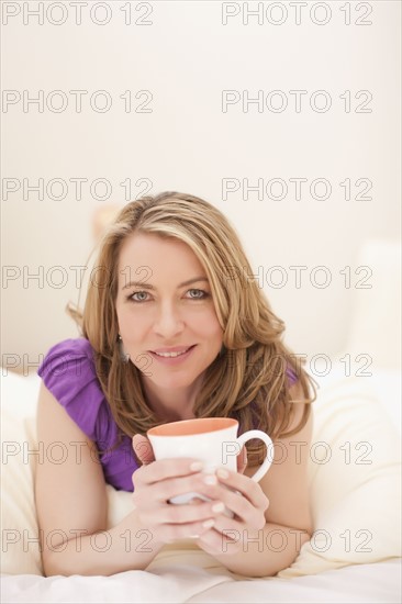 Woman lying down with a cup of coffee. Photo : Dan Bannister