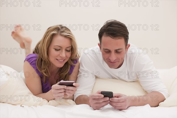 Couple lying on bed while texting. Photo : Dan Bannister