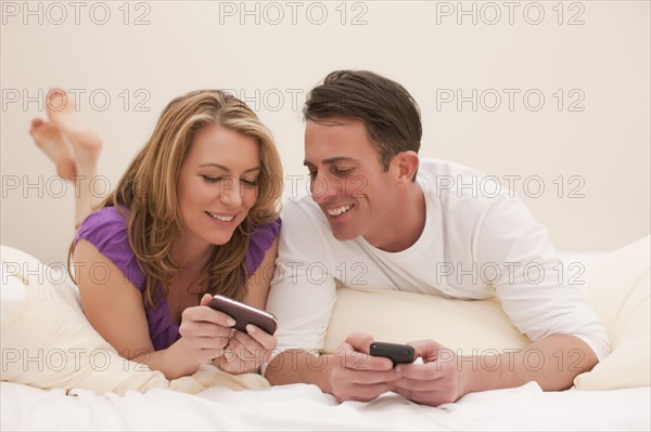 Couple looking at photo on cell phone will lying in bed. Photo : Dan Bannister