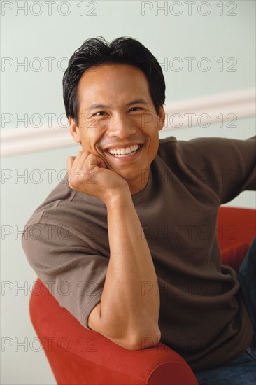 Smiling man relaxing in red chair. Photo : Rob Lewine