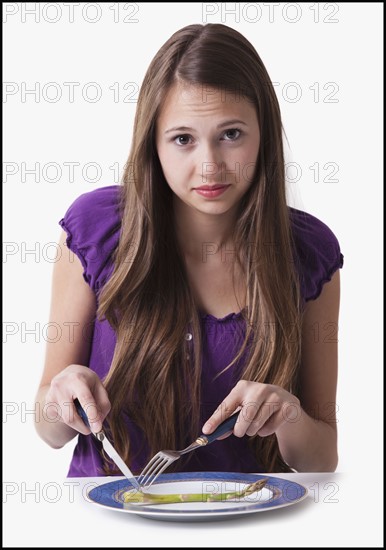 Unsatisfied teenage girl cutting a spear of asparagus. Photo : Mike Kemp