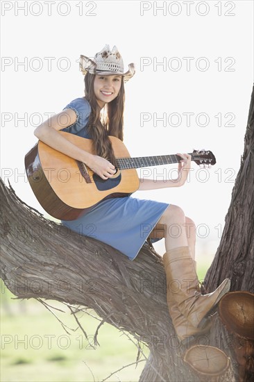 Cowgirl sitting in tree playing guitar. Photo : Mike Kemp