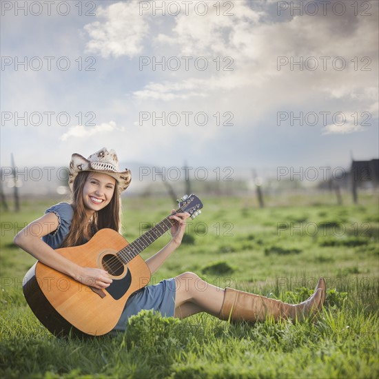 Cowgirl sitting in field playing guitar. Photo : Mike Kemp