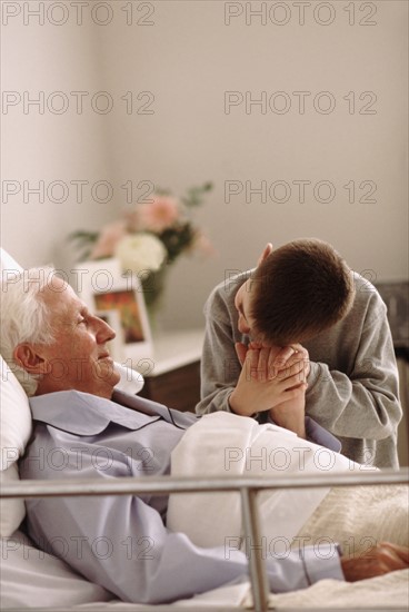 Grandfather lying in hospital bed as his grandson holds his hand. Photo : Rob Lewine