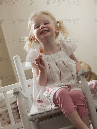 Young girl in rocking chair eating a sucker. Photo : Mike Kemp