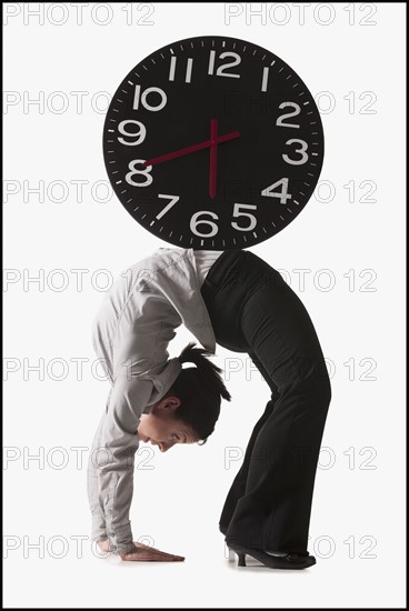 Clock on top of businesswoman bending over backwards. Photo : Mike Kemp