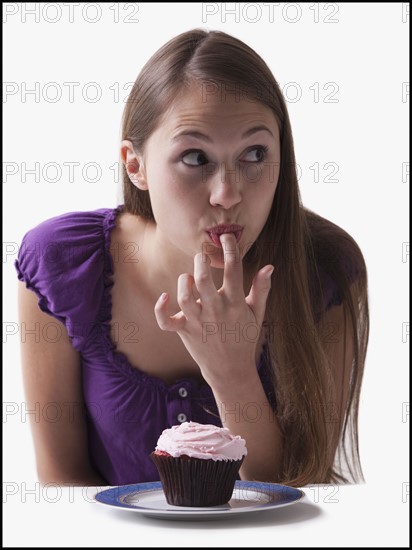 Woman sneaking a lick of icing from a cupcake. Photo : Mike Kemp