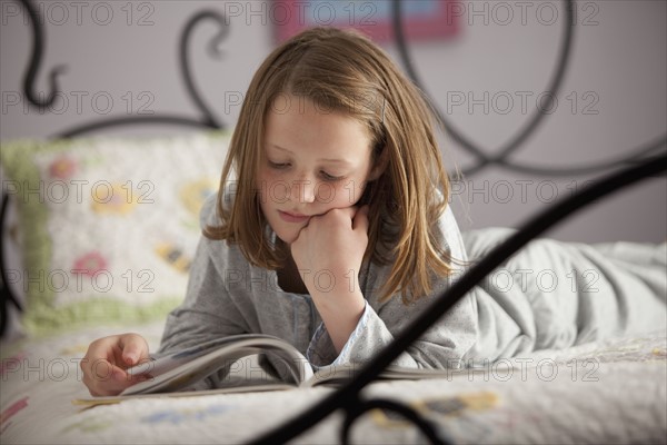 Young girl reading on her bed. Photo : Mike Kemp