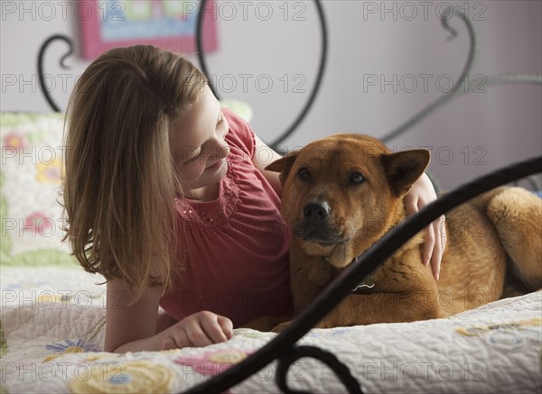 Young girl lying on bed with dog. Photo : Mike Kemp