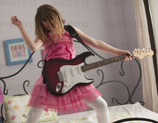 Young girls playing guitar on her bed. Photo : Mike Kemp