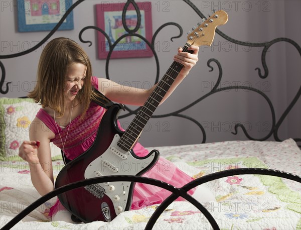 Young girls playing guitar on her bed. Photo : Mike Kemp