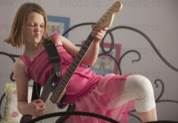 Young girls playing guitar on her bed. Photo : Mike Kemp