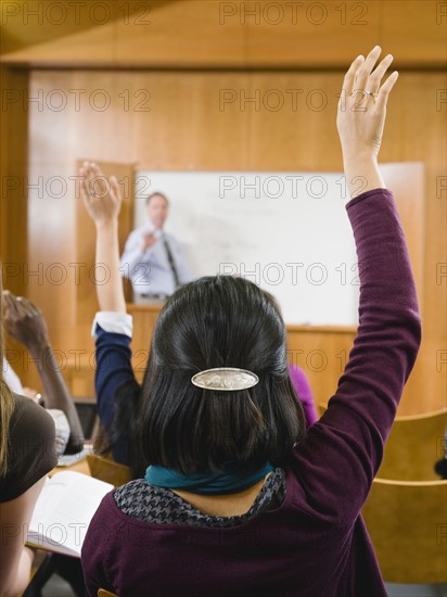 College students raising their hands in lecture hall.