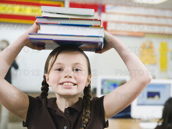 Elementary student holding a stack of books on her head.