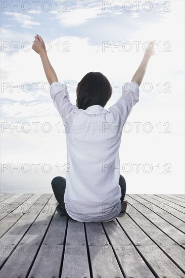 Woman sitting on porch with her arms raised. Photo : momentimages