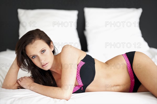 Woman wearing bra and underwear lying on bed. Photo : momentimages