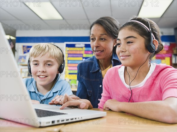 Teacher helping students use laptop.