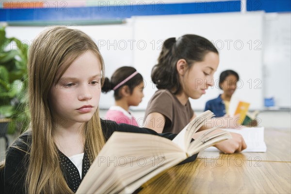 Elementary school students reading books at desk.