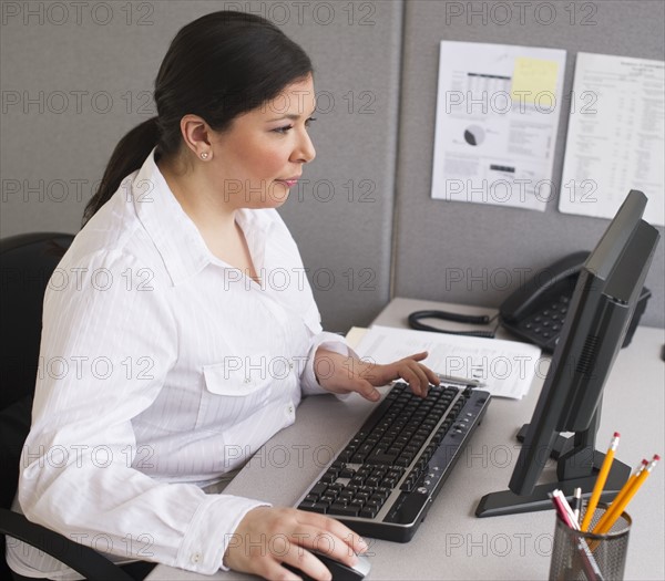 Businesswoman working on laptop in cubicle.