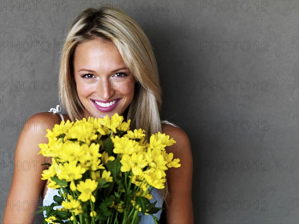 Pretty blond woman holding a bouquet of flowers. Photo : momentimages