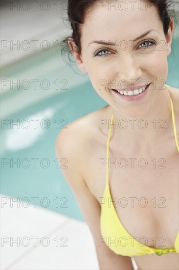 Bikini clad woman standing next to pool. Photo : momentimages