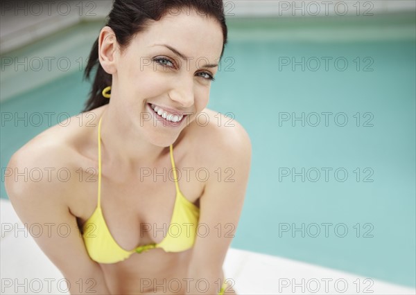 Woman wearing bikini sitting beside pool. Photo : momentimages