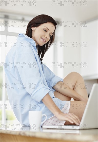 Beautiful brunette sitting on kitchen counter. Photo : momentimages