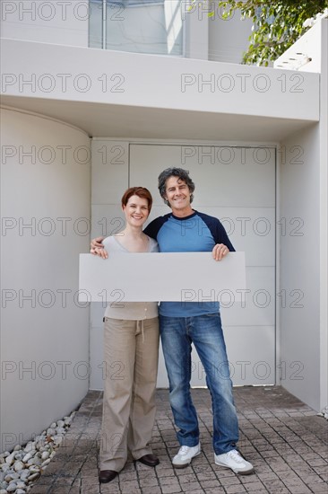 Couple standing in front of their home. Photo. momentimages