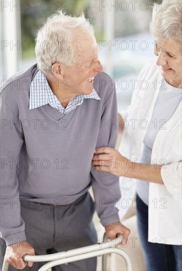 Senior woman assisting man with a walker. Photo : momentimages