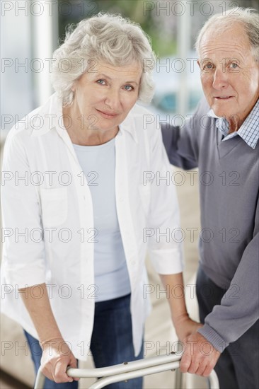 Senior man assisting woman with a walker. Photo : momentimages
