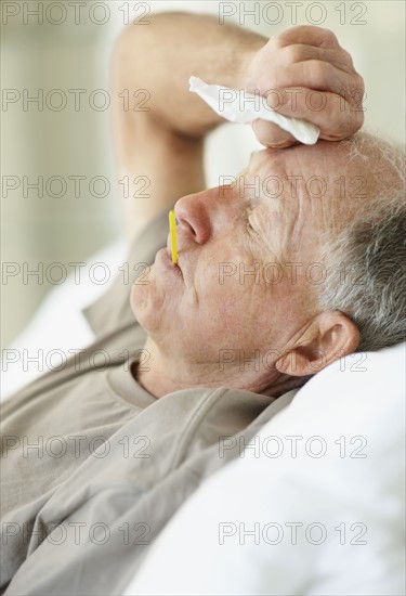 Senior man with a thermometer in his mouth. Photo : momentimages