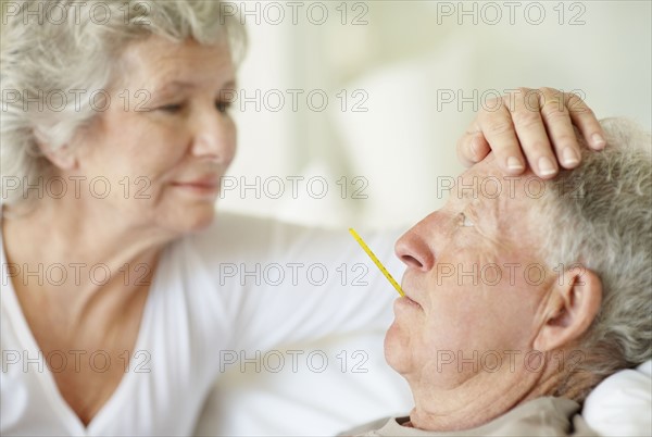 Senior woman caring for man with a fever. Photo. momentimages