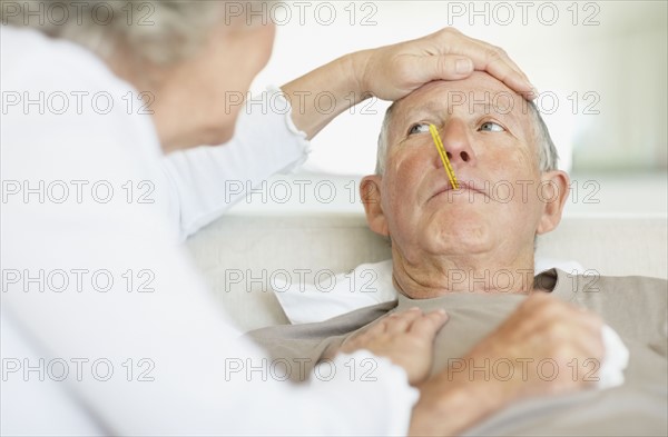 Senior woman caring for man with a fever. Photo : momentimages