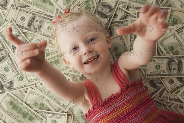 Young girl lying on a pile of money. Photo : Mike Kemp