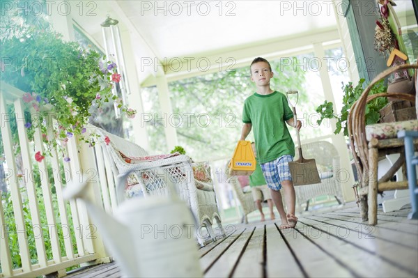 Young boy carrying shovel and tool box on porch. Photo : Tim Pannell