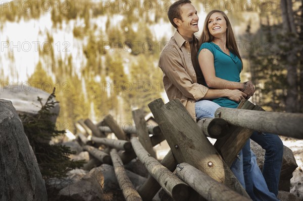 Laughing couple sitting on log fence. Photo. FBP