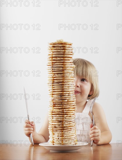 Young girl sitting behind a tall stack of pancakes. Photo. FBP