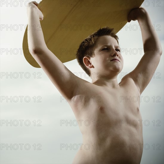 Young boy holding a surfboard over his head. Photo. FBP