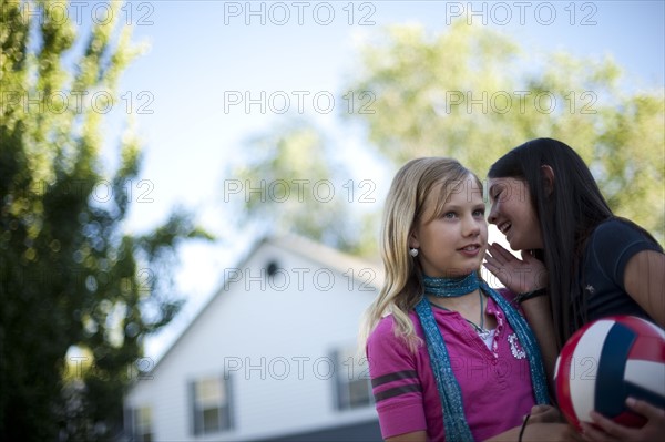 Young girl whispering to her friend. Photo. Tim Pannell