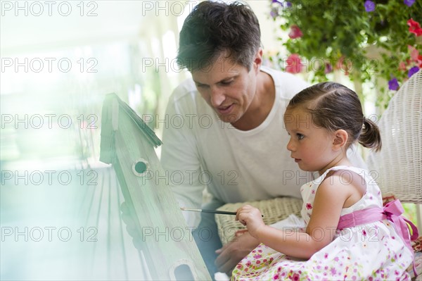 Father helping his daughter paint a birdhouse. Photo : Tim Pannell