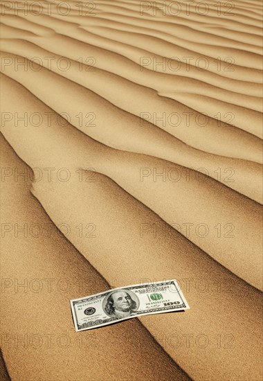 100 dollar bill on sand in desert. Photo : Mike Kemp