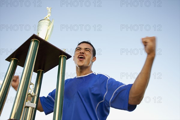 Trophy in front of cheering soccer player. Photo : Mike Kemp