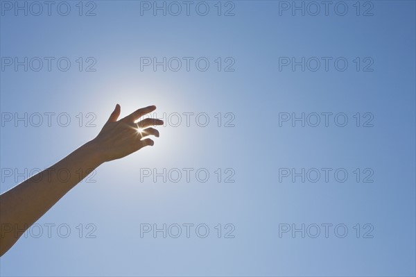 Hand in front of a sun flare in the sky. Photo. Chris Hackett