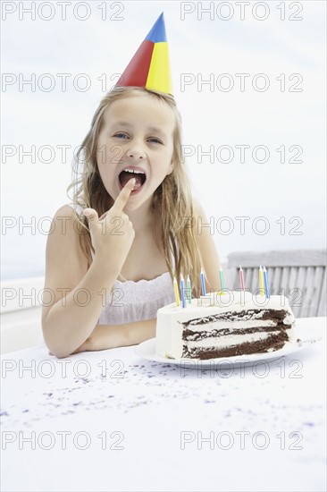Birthday girl licking icing off her finger. Photo. momentimages