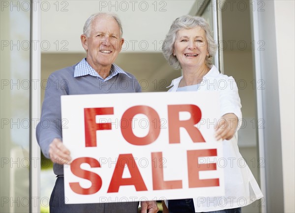 Senior couple holding for sale sign. Photo. momentimages