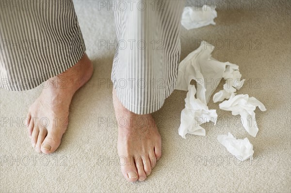 Man's feet surrounded by crumpled tissues. Photo. momentimages