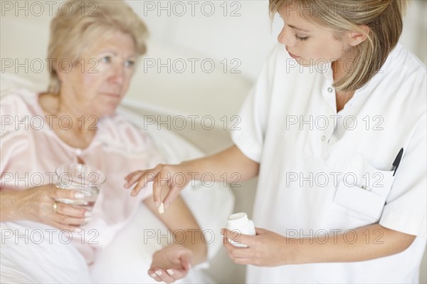 Nurse giving pill to senior woman. Photo : momentimages